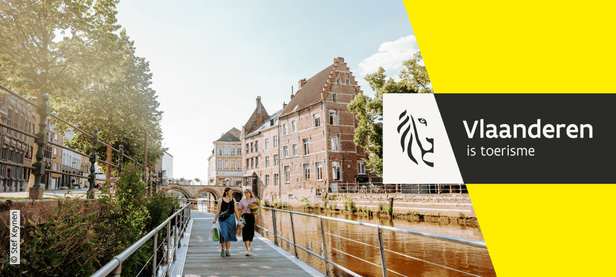 Zicht op een wandelpad langs het water in Mechelen met historische gebouwen op de achtergrond en het logo van Toerisme Vlaanderen.